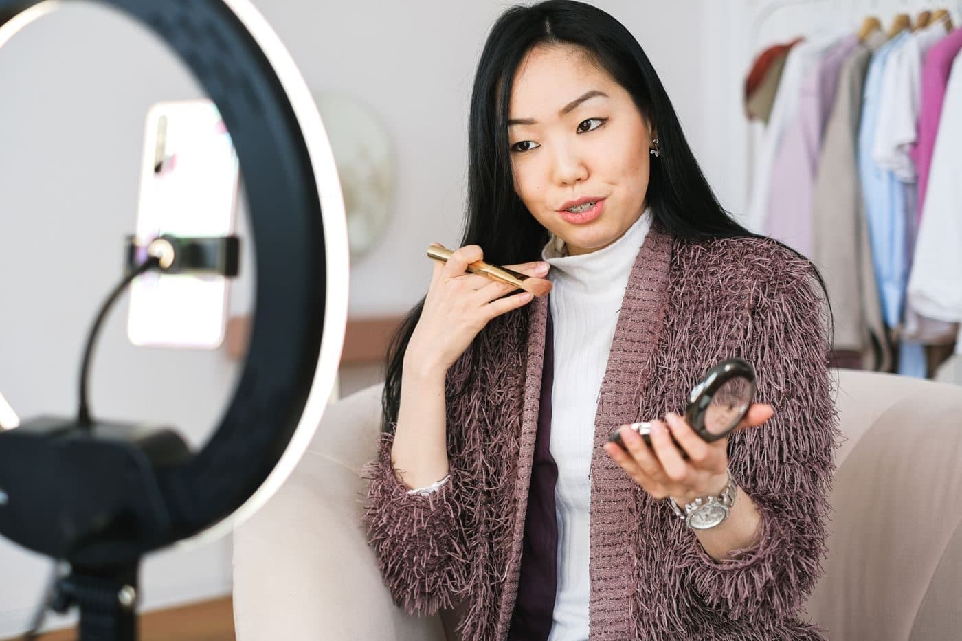 A creator in front of a ring light, applying makeup as she films herself